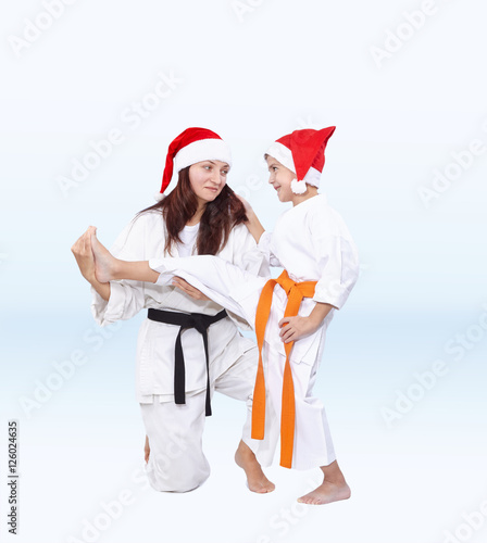 In caps of Santa Claus Mother is training the son kick leg