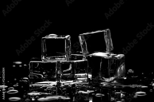 Wet ice cubes on black background with water drops and reflections