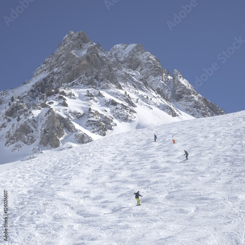 Unidentified skiers are on the snowy slope into  Grand Tourmalet ski resort against the mountain range in the French Pyrenees © aljndr