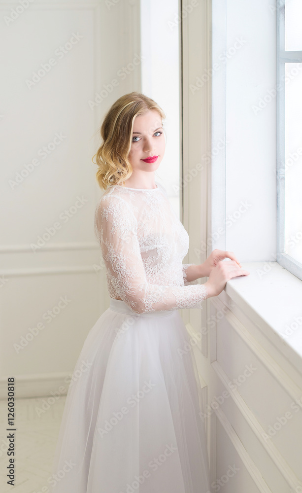 Beautiful bride standing at window in white room. Beautiful bride standing at window in white room.