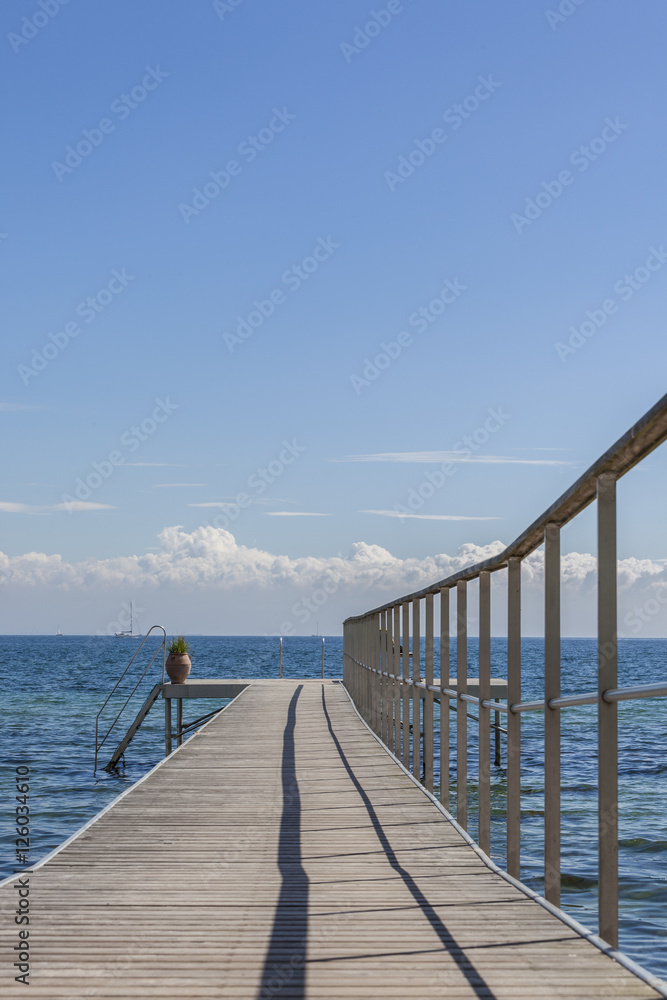 Wooden jetty with stairs into the sea sailboat on background vertical
