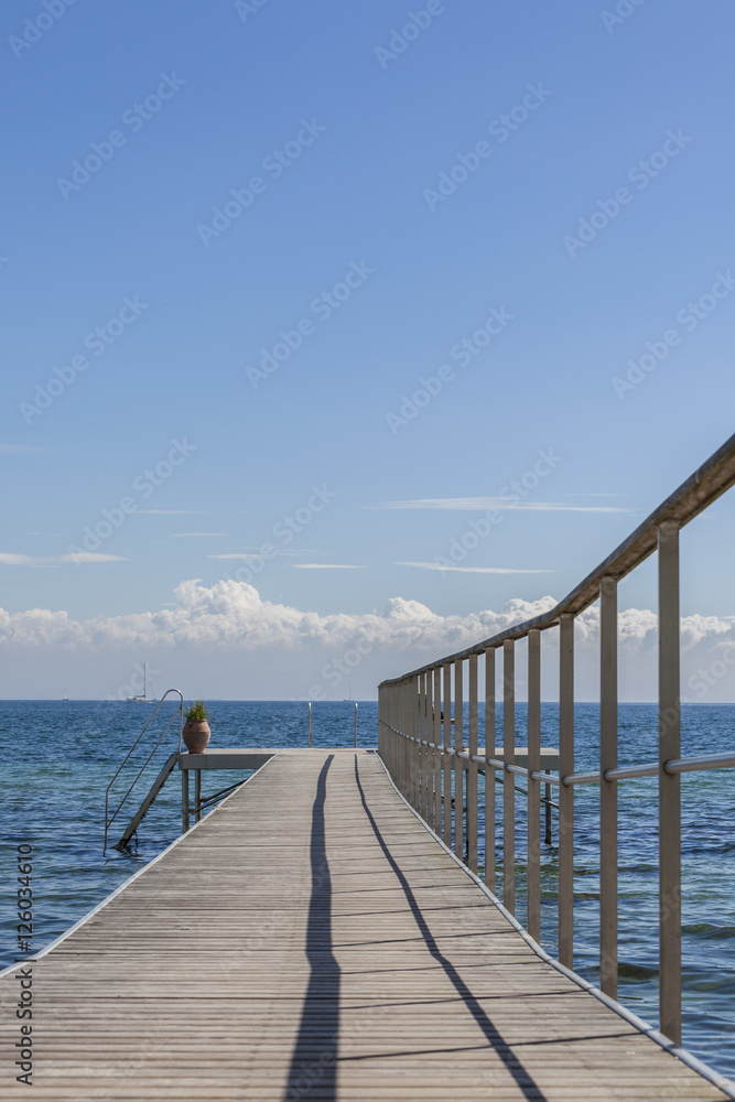 Fototapeta premium Wooden jetty with stairs into the sea sailboat on background vertical