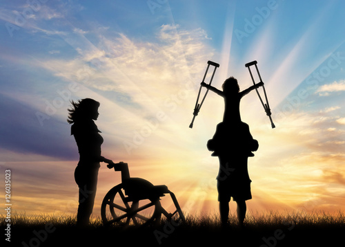 Disabled child on shoulders of father holding his crutches and wheelchair nurse sunset