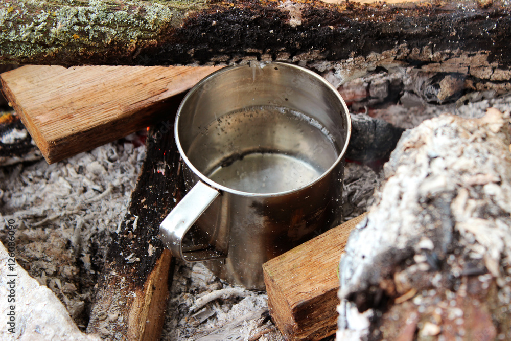 Metal mug on a stump on a background of fire. Cup on a log Metal mug on a stump on a background of fire. Cup on a log