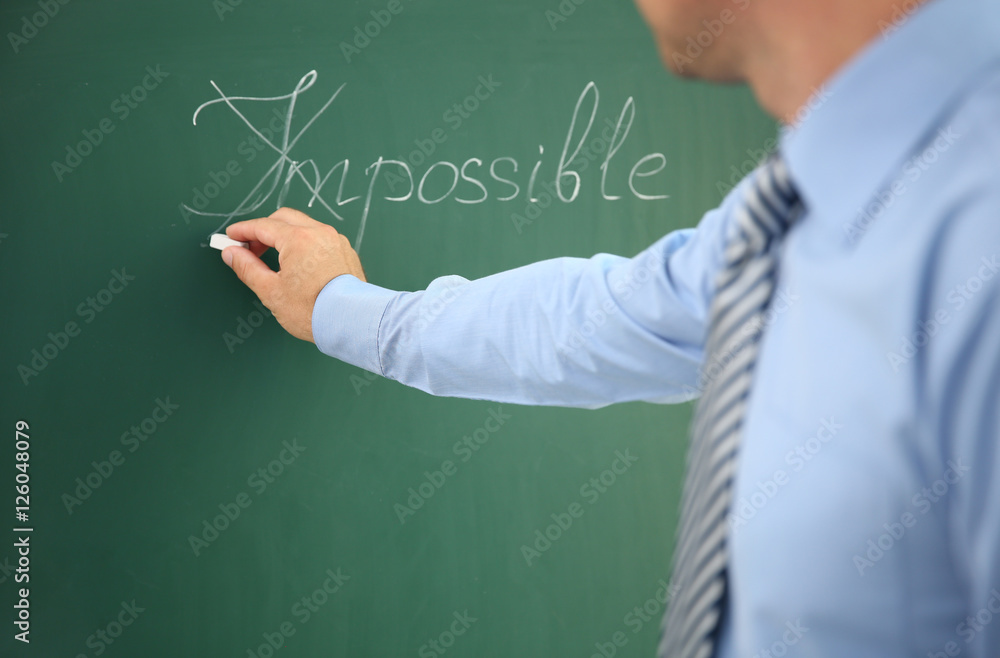 Businessman putting a cross over word impossible on blackboard Businessman putting a cross over word impossible on blackboard