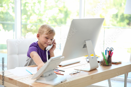 Little boy talking on phone at father's table in office
