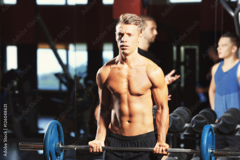 Naklejka premium Athletic man training with barbell in gym