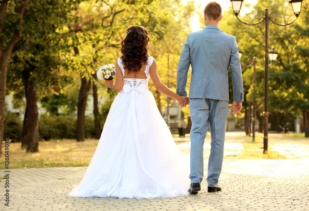 Beautiful young wedding couple holding hands while walking in park
