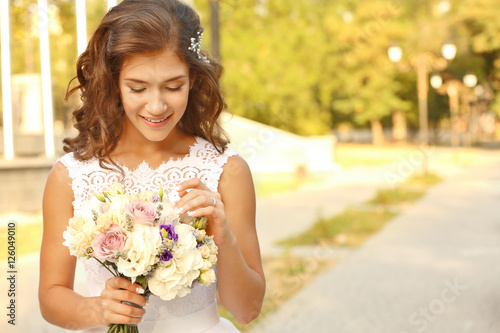 Portrait of beautiful young bride with bouquet of flowers in park