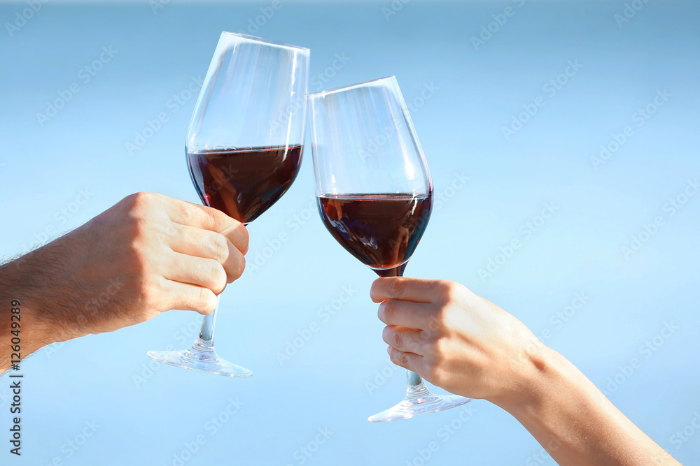 Two hands holding glasses with red wine on sea background