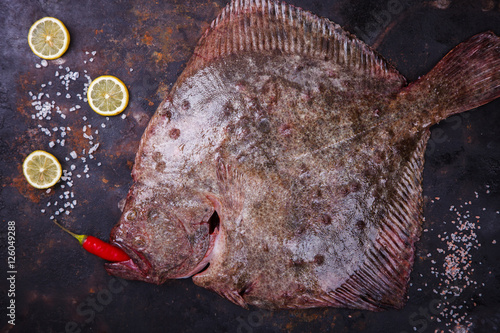 Fototapet Raw whole flounder fish with spices,  onion on dark background , top view