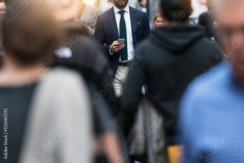 Business people walking from the job in busy city street. Elegant businessman in the people crowd walking and texting on the phone.