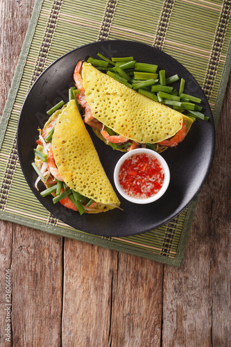 Banh Xeo crepes stuffed with pork, shrimp, onions, bean sprouts and spicy sauce closeup. vertical top view