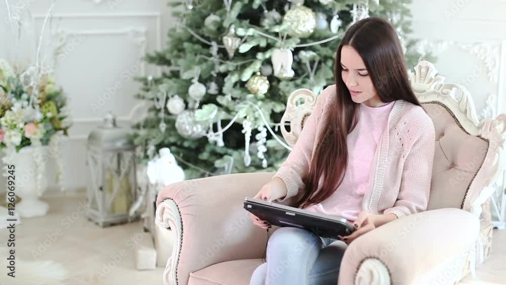 A girl sits in a chair, under the Christmas tree and working on a laptop. A girl sits in a chair, under the Christmas tree and working on a laptop.