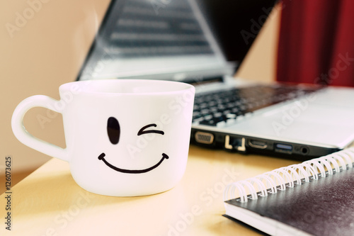 Smiling cup, notepad and laptop on the desk