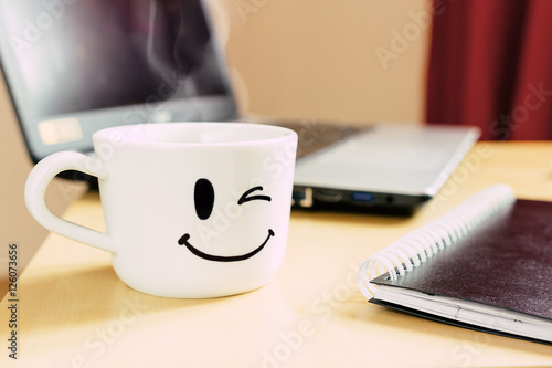 Foto Smiling cup, notepad and laptop on the desk