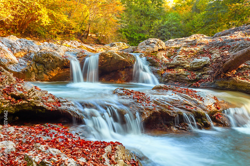 Beautiful waterfall in forest at sunset. Autumn landscape, fallen leaves, water flow 
