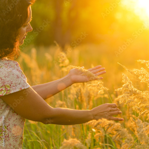Adult brunette woman in a dres touches the golden grasses on the meadow in the sunlight