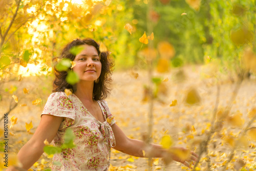 Adult brunette woman in a dress throws up dry yellow leaves in the autumn forest, sunny