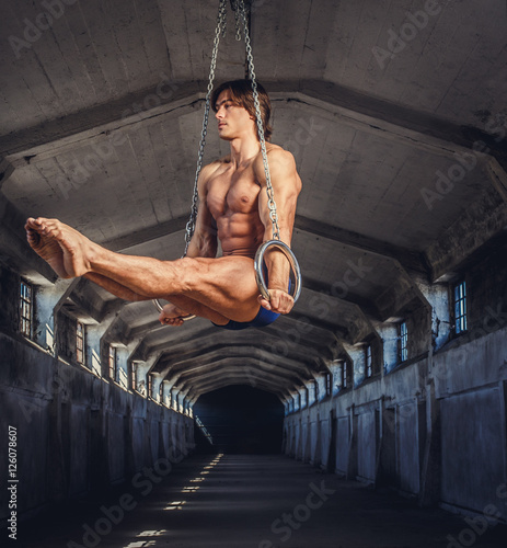 Athletic muscular male posing with gymnastic rings in a dark tunnel