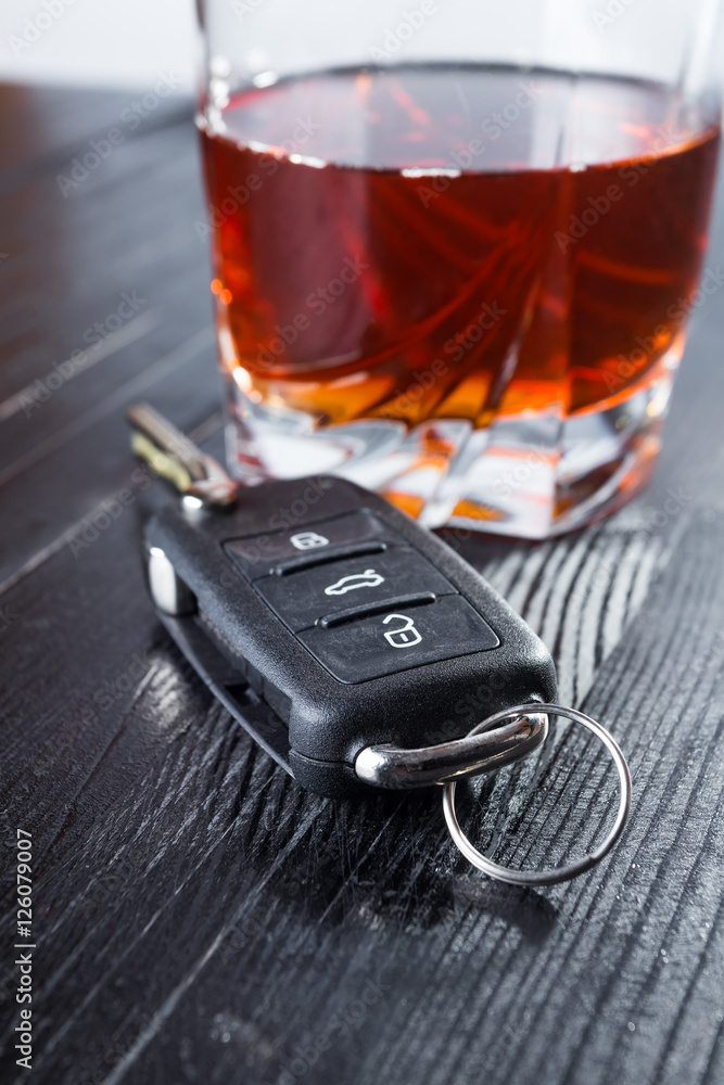 Car key and whiskey in a glass on black wooden table. Don't drink and drive abstract concept.