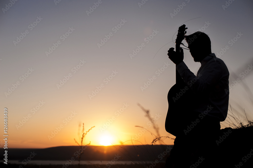 Silhouette of male guitarist playing outdoors