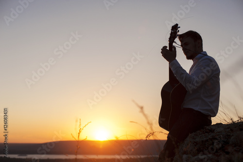 Silhouette of young guitarist playing outdoors