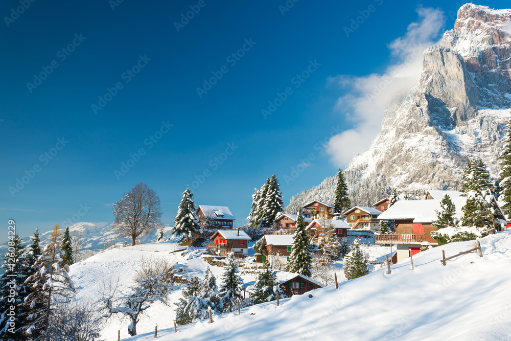 Fototapeta premium Christmas vacation in Europe. Travel to Switzerland in the winter. Alpine Village in the snow. Traditional houses with red shutters and roofs.