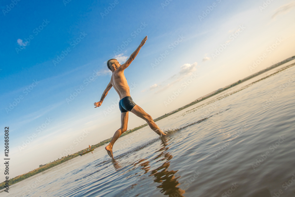 Adult man with a mohawk on his head and black shorts running on water against the backdrop of blue sky with clouds Adult man with a mohawk on his head and black shorts running on water against the backdrop of blue sky with clouds
