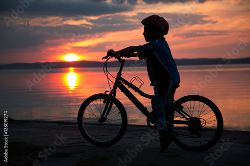 Silhouette of a young boy, at sunset, riding bicycle © Belphnaque
