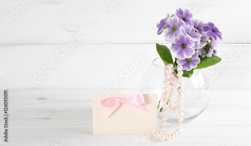 Bouquet of primroses in round vase and women s pearl necklace