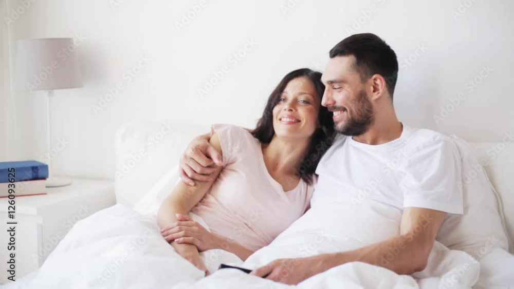 happy couple watching tv in bed at home happy couple watching tv in bed at home