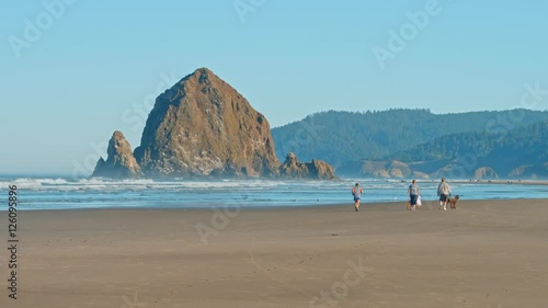 Sliding shot of people walking, jogging and walking pet dogs in the morning on Cannon Beach in Oregon with Haystack Rock in background (Pacific ocean coast)