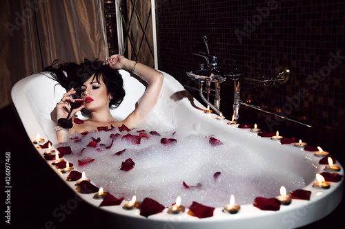 Sexy girl lying in the bath with candles and drink wine, rose pe
