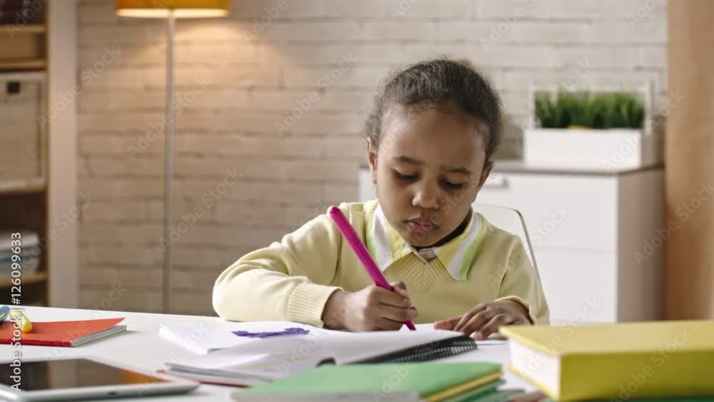 African girl sitting at the table and drawing on paper with pink felt tip pen African girl sitting at the table and drawing on paper with pink felt tip pen
