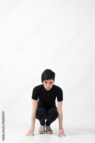 Determination concept. Casual woman in black clothes in start running position looking at camera over gray studio background with copyspace.