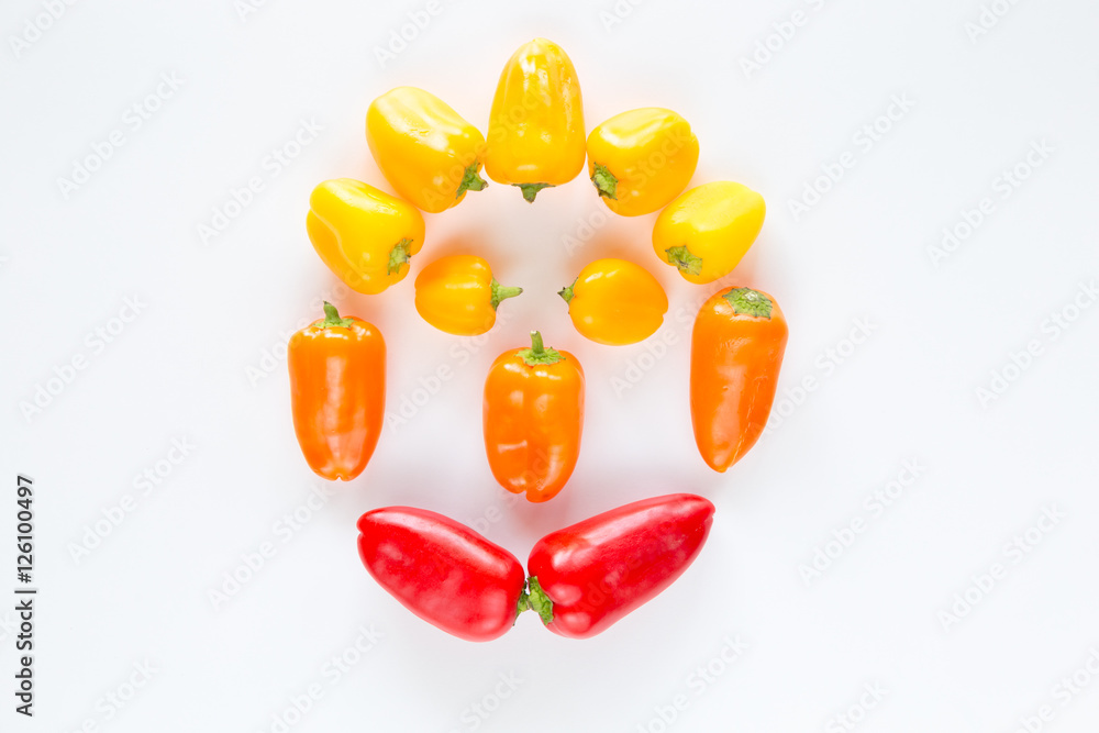 Peperoni rossi gialli e arancioni raffiguranti un viso umano su fondo chiaro