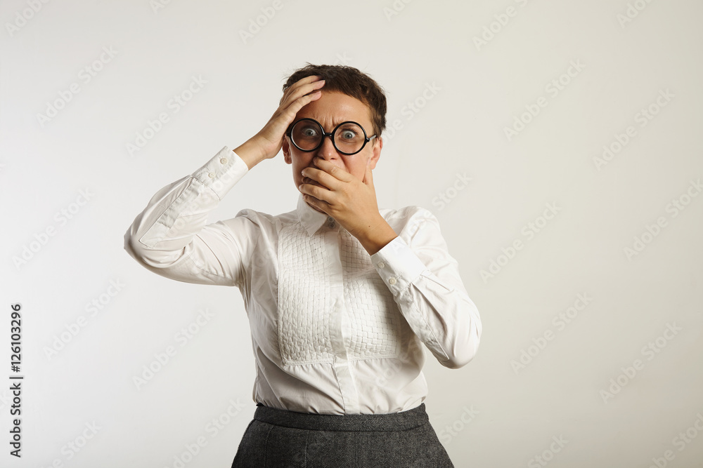 Fearful emotional young woman covers her mouth in horror isolated on white Fearful emotional young woman covers her mouth in horror isolated on white