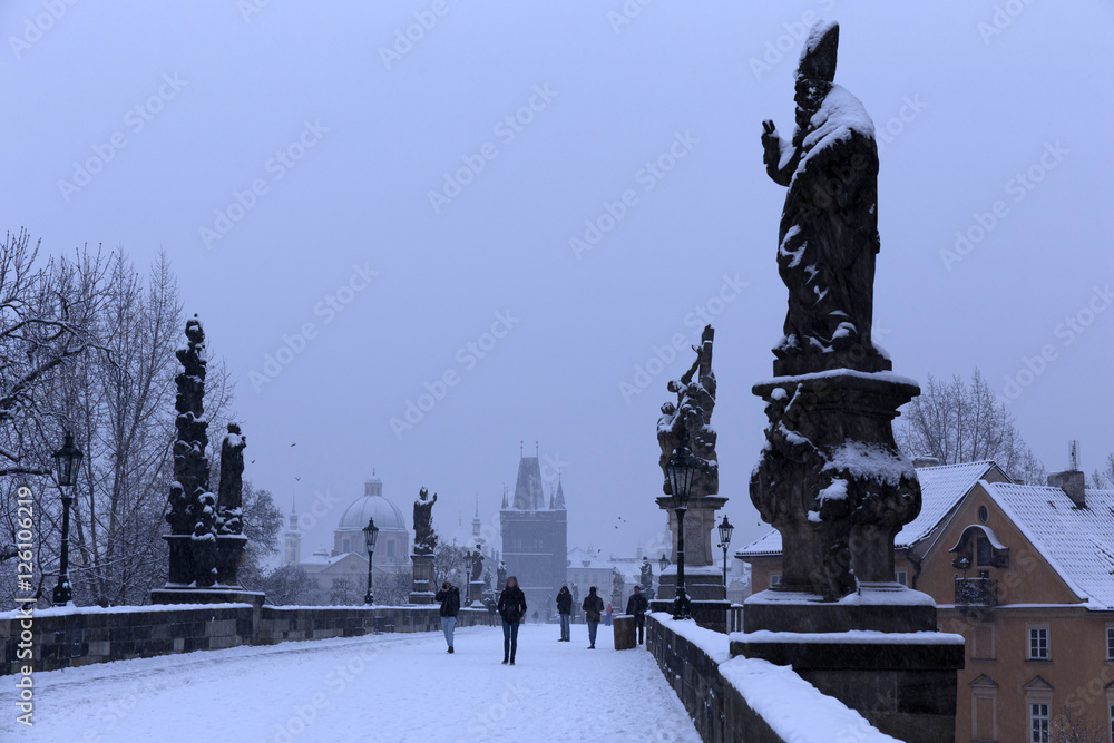 Snowy foggy Prague Old Town with Bridge Tower and St. Francis of Assisi Cathedral from Charles Bridge with its baroque Statues, Czech republic