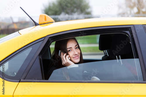Beautiful brunette talking on phone in open window of taxi