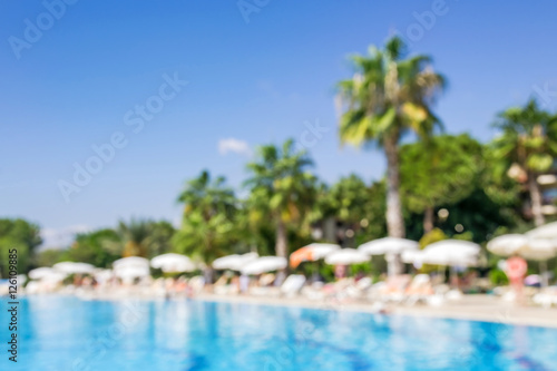 Fototapeta Naklejka Na Ścianę i Meble -  Swimming pool with palm trees on a sunny summer day. Abstract blurred vacation background