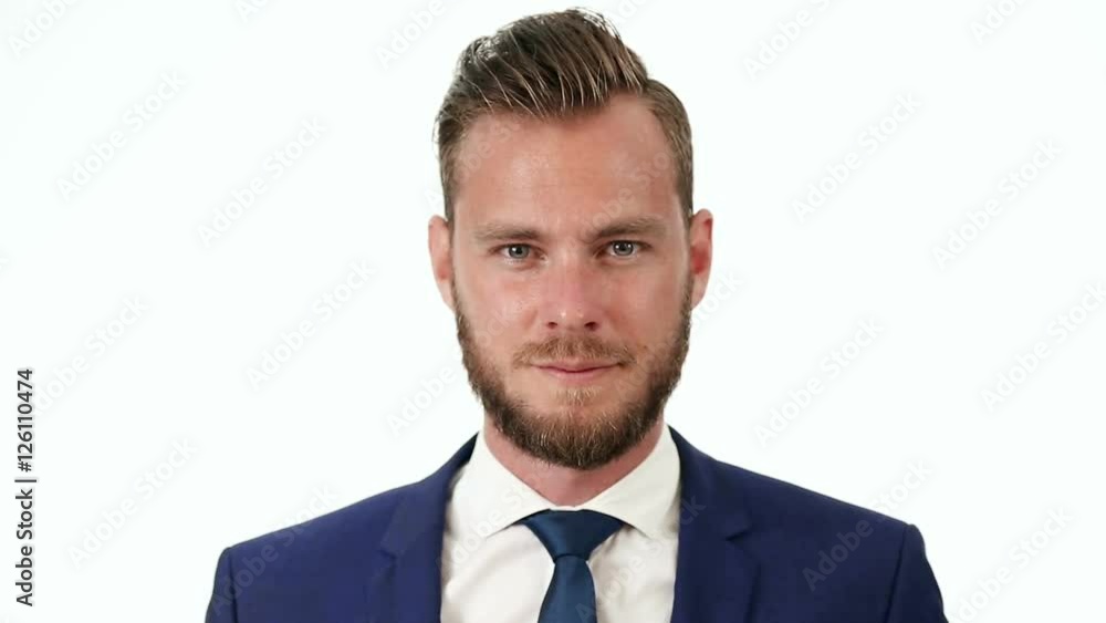 Video of a handsome businessman wearing a blue suit, blue tie and white shirt, standing in front of a white background.