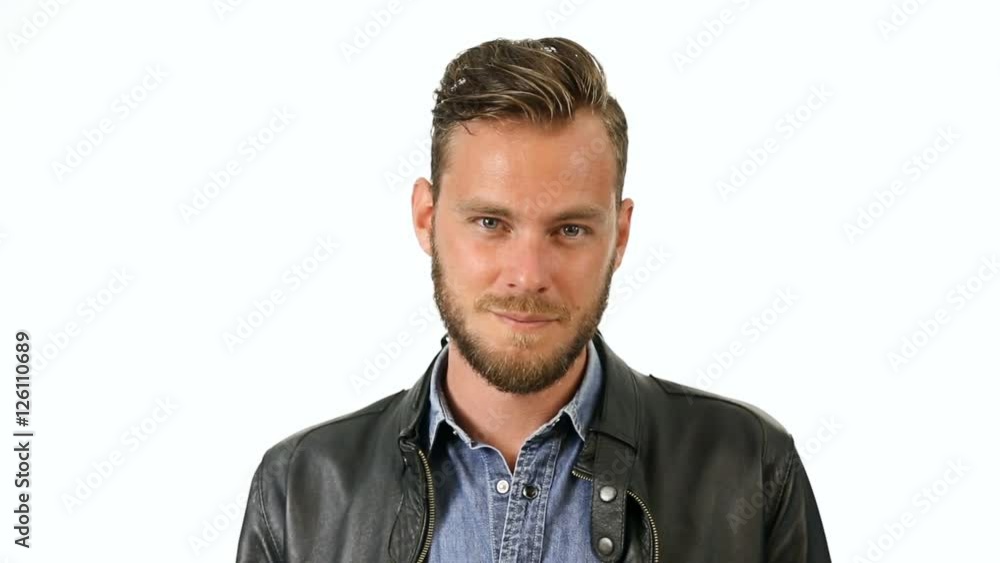 A handsome man wearing a black leather jacket and jeans shirt moving in front of a white background smiling. A handsome man wearing a black leather jacket and jeans shirt moving in front of a white background smiling.