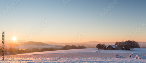 Fototapeta Naklejka Na Ścianę i Meble -  Schneelandschaft mit bedeckter Schneedecke und Gegenlicht bei Sonnenaufgang