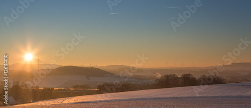 Schneelandschaft mit bedeckter Schneedecke und Gegenlicht bei Sonnenaufgang