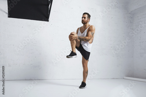 Athletic young man doing knee raises  stretching his legs