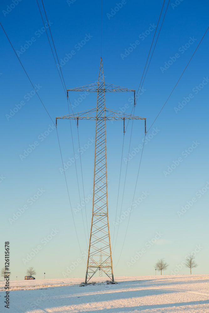 Winterlandschaft mit Oberleitungen für Strom im Gegenlicht bei blauem Himmel