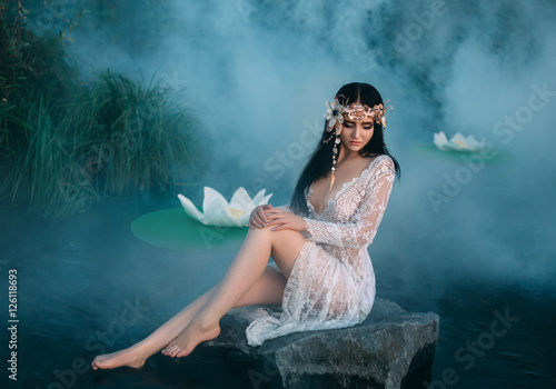 Charming, sexy lady sitting on a huge stone in water