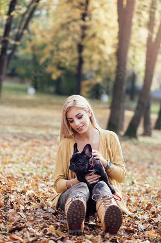 Beautiful and happy woman enjoying in autumn park with her adorable French bulldog.
