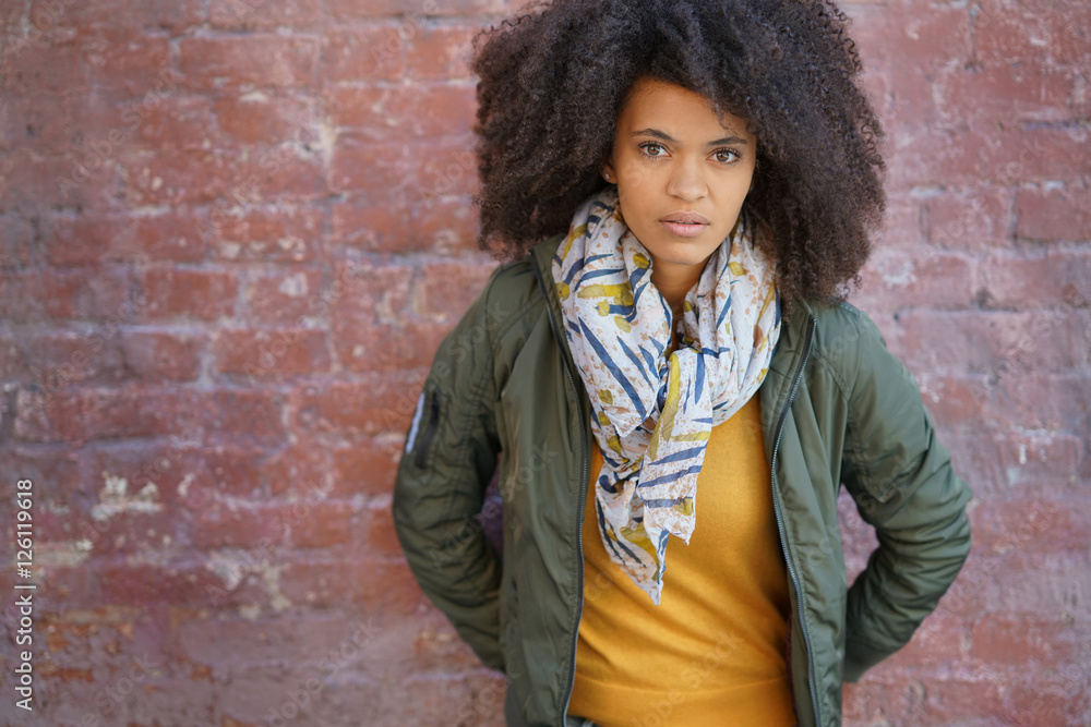 Trendy mixed-raced girl standing by brick wall Trendy mixed-raced girl standing by brick wall